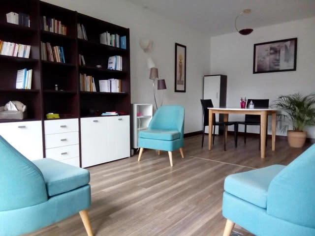 La salle de consultation : trois fauteuils turquoise, une bibliothèque et une table de travail